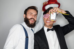 Content young multiracial male friends in stylish classy clothes smiling brightly and taking photo with film camera during party